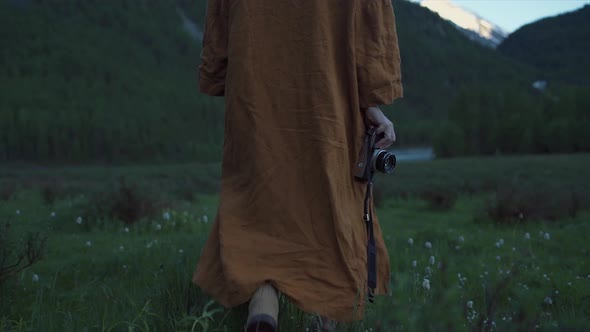 Back shot following a Person walking in nature wearing a orange robe holding a camera