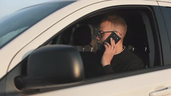 A Man is Sitting in a Car and Talking Emotionally on the Phone