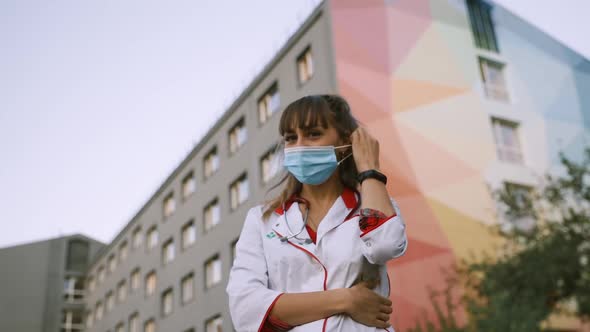 Cheerful Young Doctor at Hospital Takes Off Surgical Face Mask and Smiles