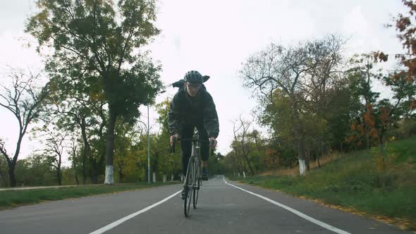 Young Hipster Man in Helmet Riding Fixed Gear Bicycle in Park During Autumn Morning