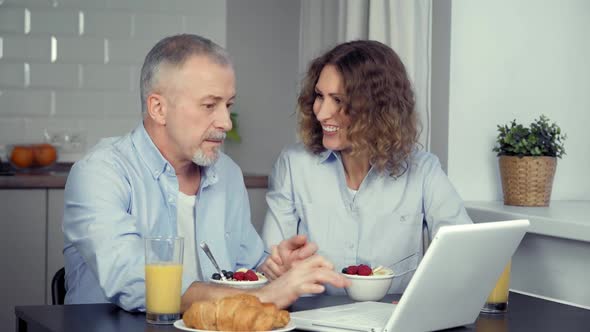 A Happy Middleaged Couple Talking Together and Shopping Online on a Laptop