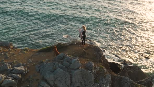 4k drone Slow motion Surfer with board. Slim woman in swimsuit looking at the beach on the cliff wit