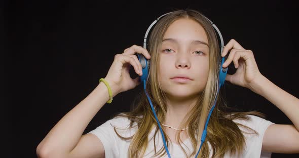 Teenage Girl Wearing Headphones and Listening to the Hard Rock Music Over Black Background
