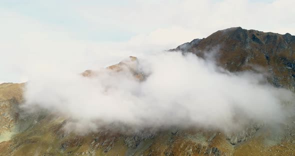 drone lifting up through the clouds to the top of the mountain on a sunny day. rock in the clouds