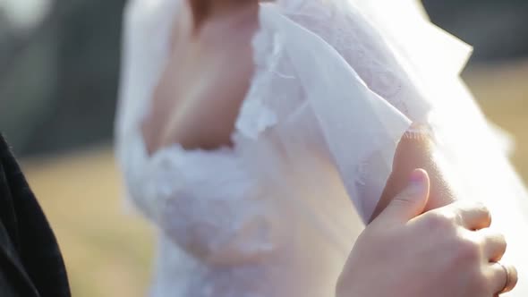 Young Bearded Groom Strokes His Bride By the Hand on the Nature, Focusing on the Girl, Close View