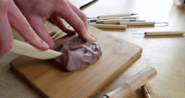 An artist carving cutting brown modeling clay off off a sculpture with a wooden tool in a messy art