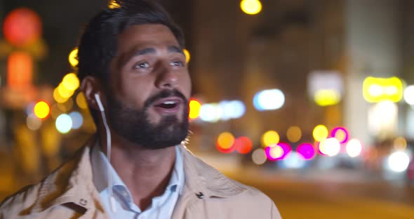 Bokeh Shot of Handsome Man Listening to Music in Earphones and Singing Outdoors