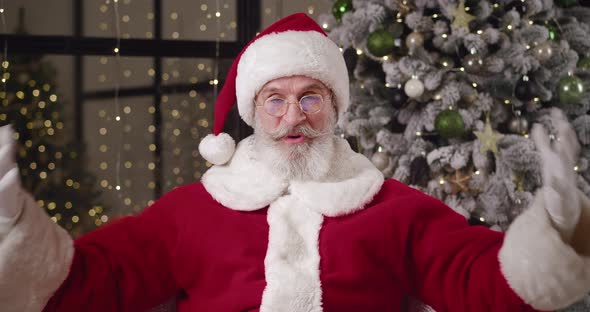 Cheerful Elderly Man in Santa Claus Costume Sits in Front of a Web Camera Against a Decorated