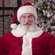 Cheerful Elderly Man in Santa Claus Costume Sits in Front of a Web Camera Against a Decorated - VideoHive Item for Sale