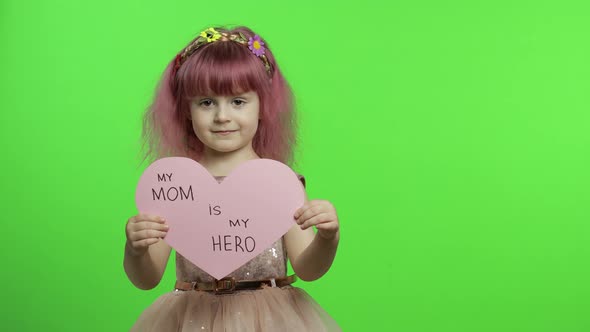 Child Girl Princess Holds Pink Paper Heart with Text About Mother. Mother's Day