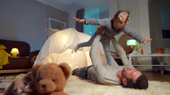 Happy Daughter Imitating Flying in Father Hands and Hugging Parent Smiling Lying at Tent in Living