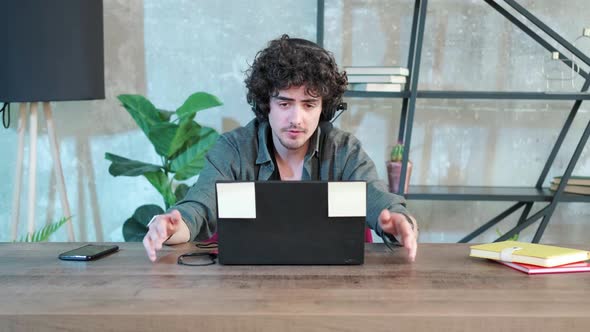 Young Curly Haired Man Using Laptop Computer with Headset to Talking Online