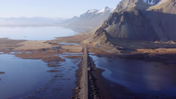 Aerial Over an Empty Dirt Road Along Fjord and Mountains