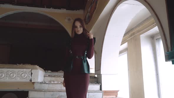 Young Pretty Girl, Dressed in Leather Wings and a Leather Skirt, Descends the Stairs in an Abandoned