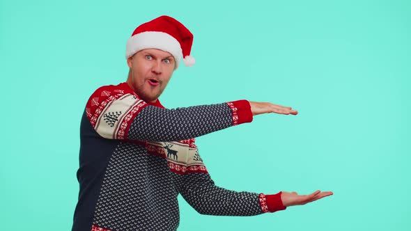 Man Wears Red New Year Sweater Deer Showing Thumbs Up and Pointing at on Blank Advertisement Space