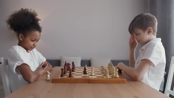 Children in Selfisolation an African Girl and a Caucasian Boy Play Chess Sitting in the Living Room