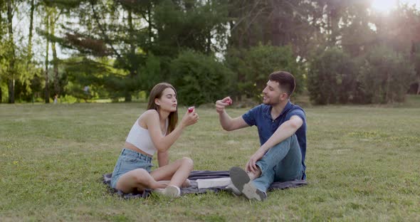 Couple Sitting on a Blanket on the Grass in the Woods and Eating Sushi Rolle with Their Hands