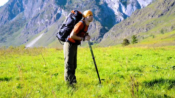 Hiking Man Walking on Green Mountain Meadow with Backpack. Summer Sport and Recreation