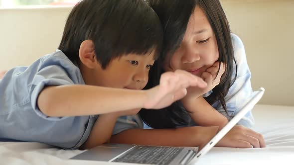 Cute Asian Children  Lying In Bed And Using Laptop On White Bed