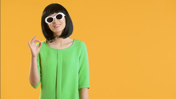 Portrait of Cute Young Woman in Retro 60's Style Showing Ok Sign with Smile Over Yellow Background