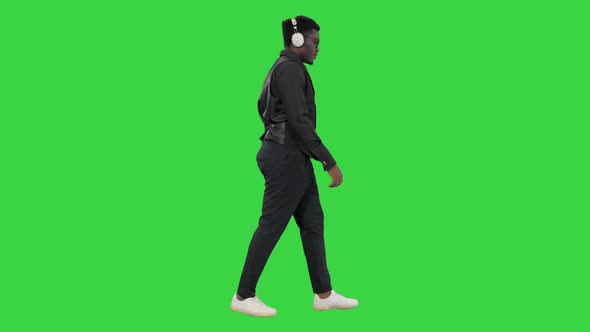 Young African American Man Listening To Music in Headphones While Walking on a Green Screen, Chroma