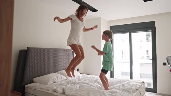Happy Mom Have Fun Jumping with Little Son on Bed