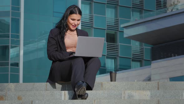 Young Happy Businesswoman Spends Leisure Sitting Outdoors on City Building Background Joyful