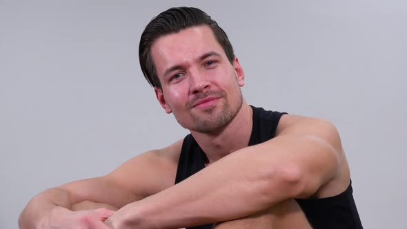 A Young Handsome Man in a Tanktop Sits and Smiles at the Camera, Closeup, White Background