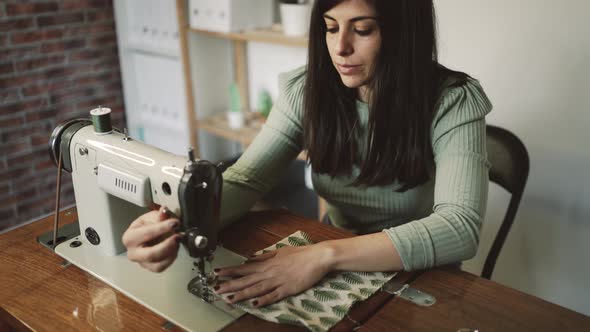 Crop seamstress pulling out thread of sewing machine in atelier