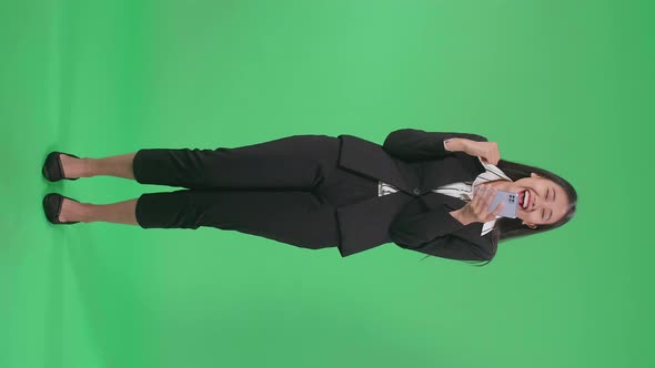 Full Body Of A Laughing Asian Business Woman Looking At The Phone Screen On Green Screen Studio