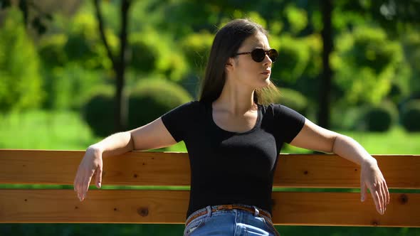 Self-Confident Woman in Dark Sunglasses Sitting on Bench in Park Looking Around