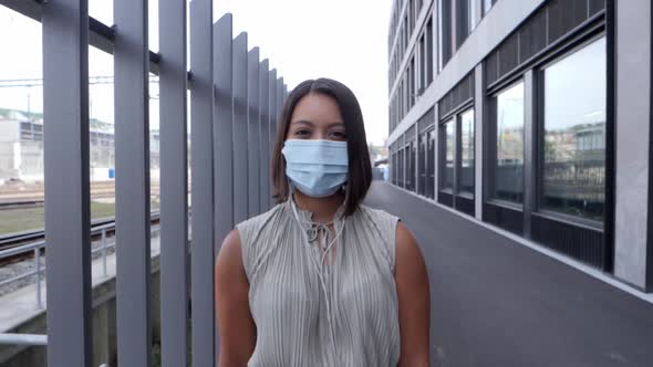 Young woman standing between metal grille with a hygienic respirator mask over her nose and mouth -