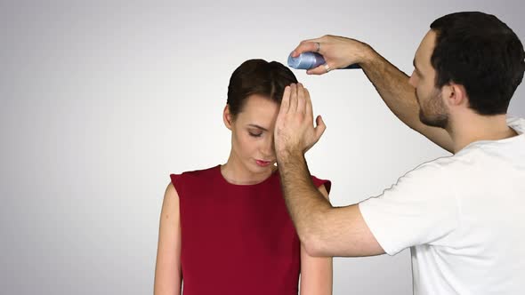 Beauty, Hairstyle and People Concept - Young Woman with Hairdresser with Hair Spray on Gradient