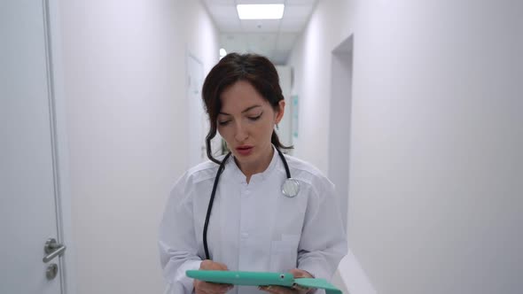 Portrait of Worried Concentrated Young Female Doctor Walking with Tablet in Slow Motion Sighing