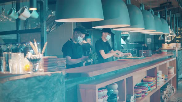 Chefs in Face Masks are Cooking in the Open Restaurant Kitchen