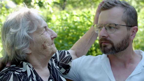 an Old Woman Strokes on the Head of Her Adult Relative Grandson with an Intelligent Look and Similar