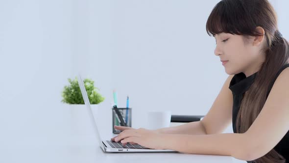 Beautiful young freelance asian woman smiling working and typing on laptop computer at desk office.