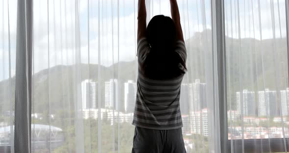 Woman stretching arm and open window curtain 