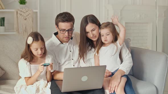 A Happy Family Uses a Laptop for Online Shopping, Sitting on the Couch at Home