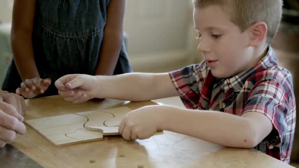 Young girl and boy in wood shop with older man finishing a wood puzzle.