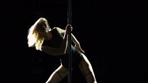 Young Sexy Slim Woman Dancing Near a Pole on a Black Studio Background