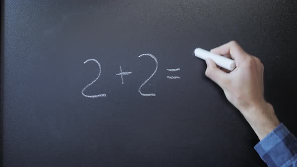 Professor writing on blackboard mathematical formulas with chalk. 2+2=4