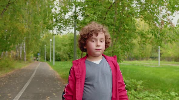 Young Curly Boy Walking on Road in Summer Park