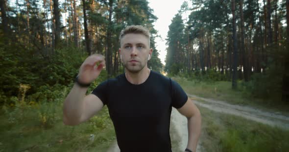 Front View of Active Man Running Among Green Trees