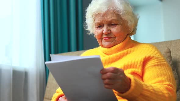 Shoked Amazed Old Woman White Grayhaired Sitting on the Sofa in Living Room with Bills