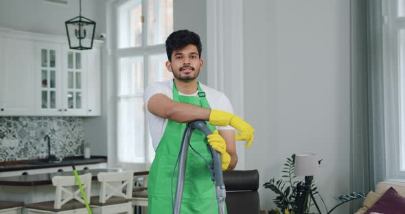 Bearded Man-Worker of Cleaning Service Leaning on Vacuum Cleaner and Looking at Camera