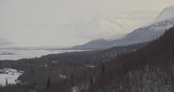 Aerial helicopter shot, track overhead icy frozen stream in valley, surrounded by barren trees and s