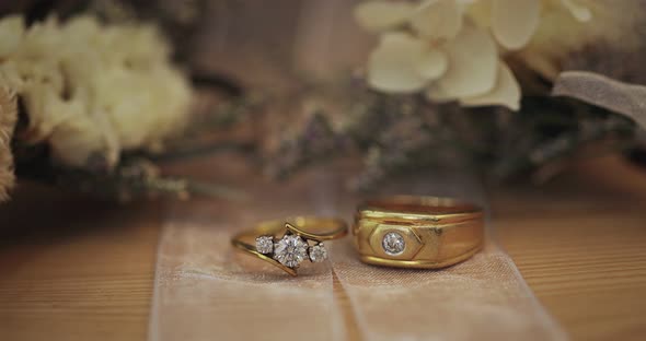 Golden Wedding Rings With Diamonds Lie Beside Flower In Bridal Bouquet.