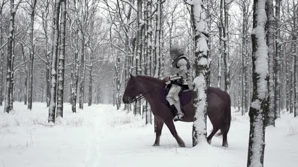 Portrait of Medieval Horseman Wearing Steel Armor Riding Through Winter Forest Among Snowy Trees in