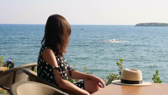 Brunette Girl, Sits at a Table in a Cafe, on the Seashore, Admires the Seascape. Hot Summer Day.